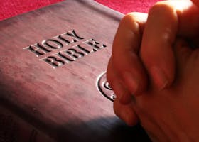 Close-up of hands praying on a Holy Bible, symbolizing faith and spirituality.