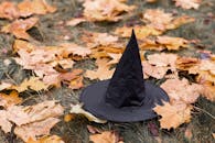 A black witch hat laying on fallen autumn leaves, creating a Halloween vibe.